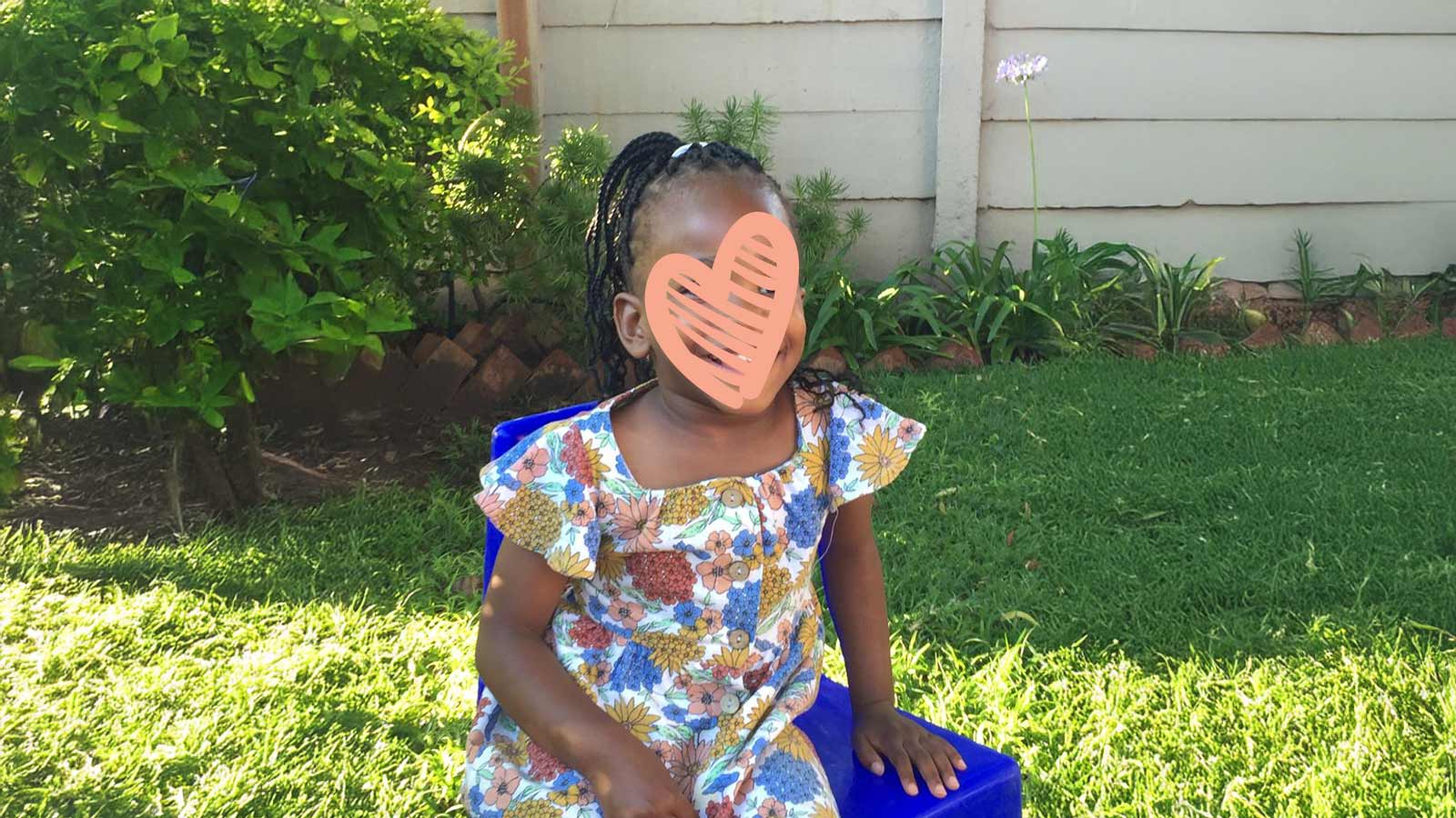 a waiting child sits in a grassy lawn in a floral dress