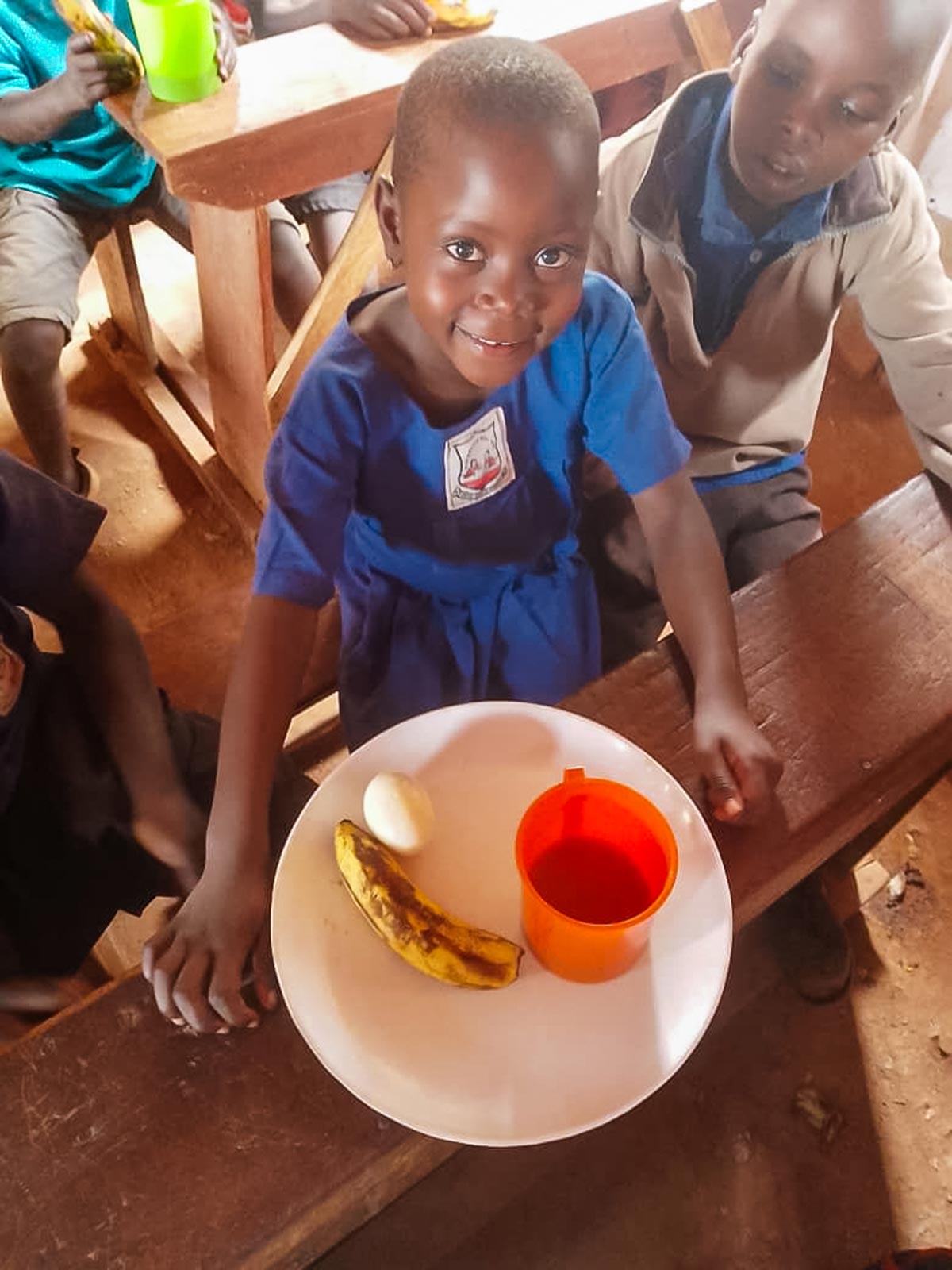 a little girl in Uganda smiles with her school lunch