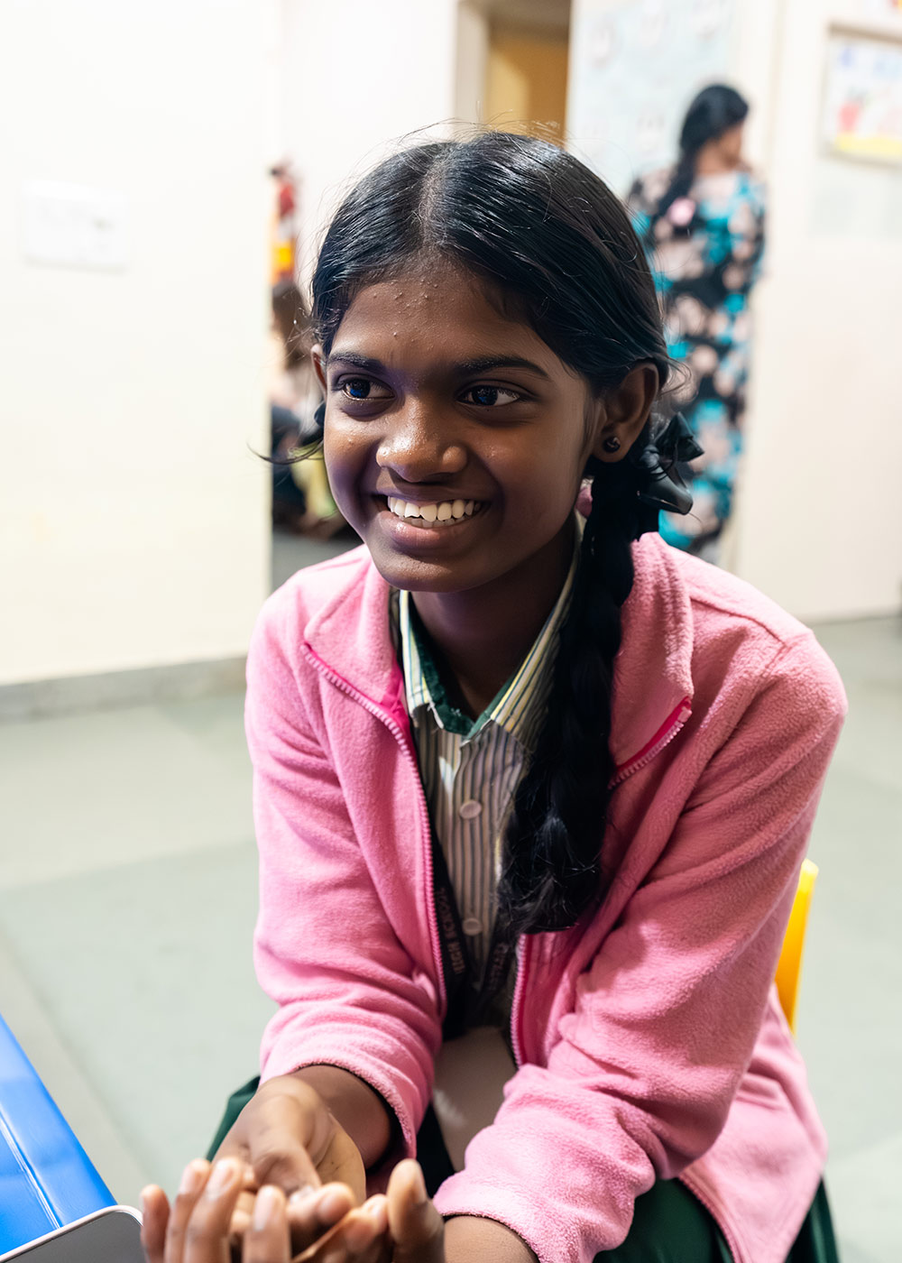 a sponsored girl in a school uniform and pink jacket speaks in a preschool classroom