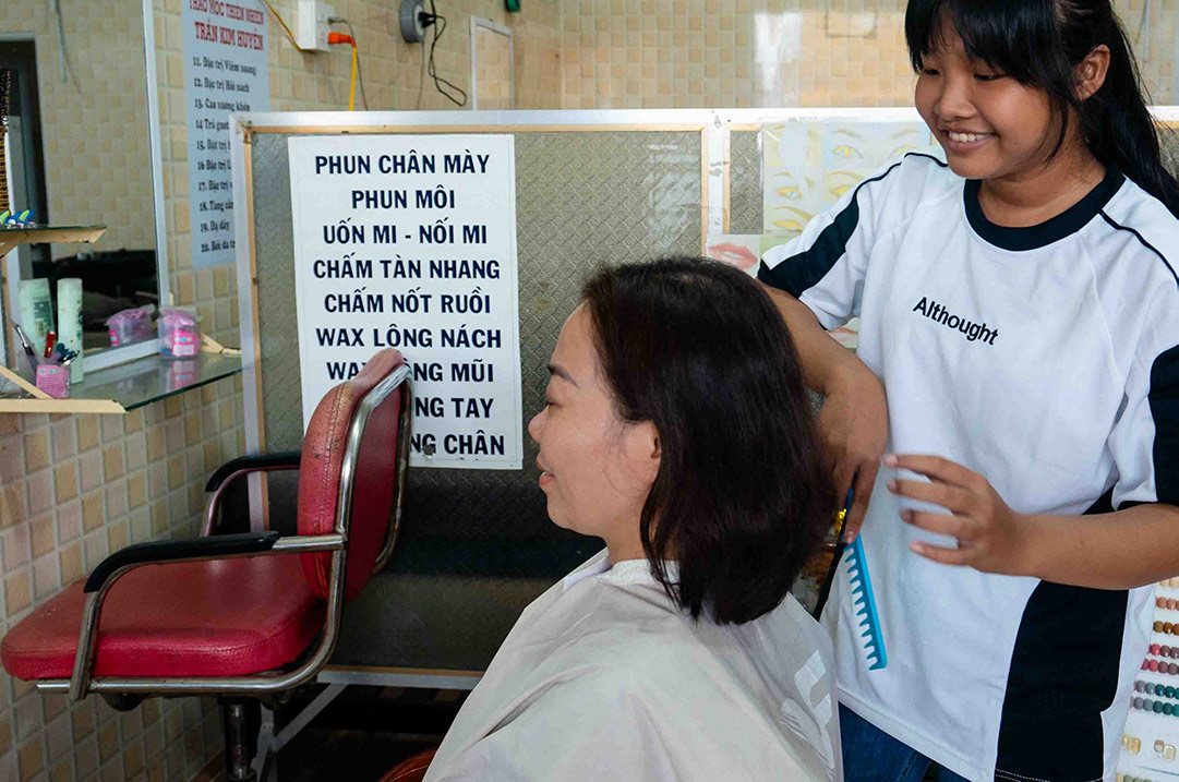 A teenage girl brushes a woman's hair in a hair salon