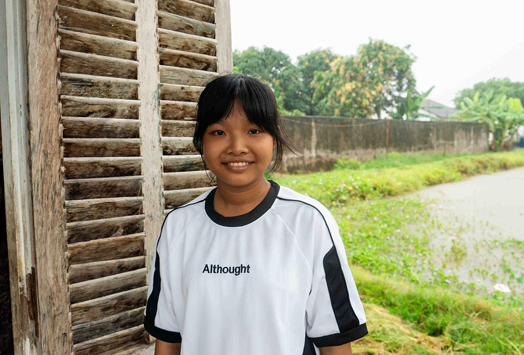A teenage girl in Vietnam smiles at the camera outside her home