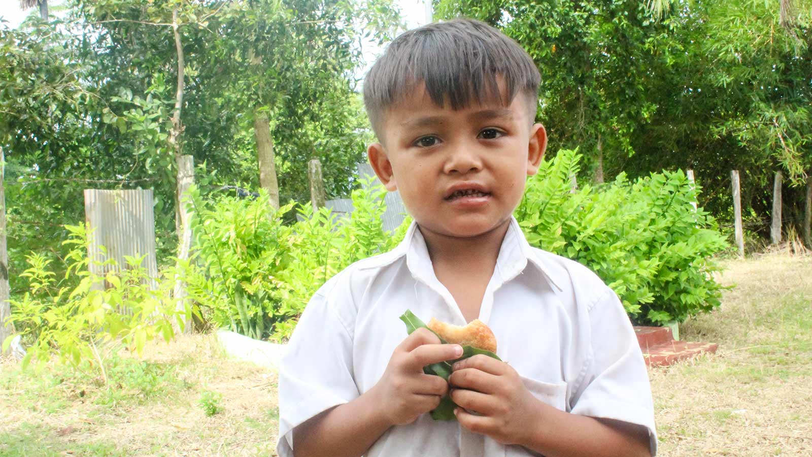 a boy holds a snack outside in Cambodia, thanks to the support of donors