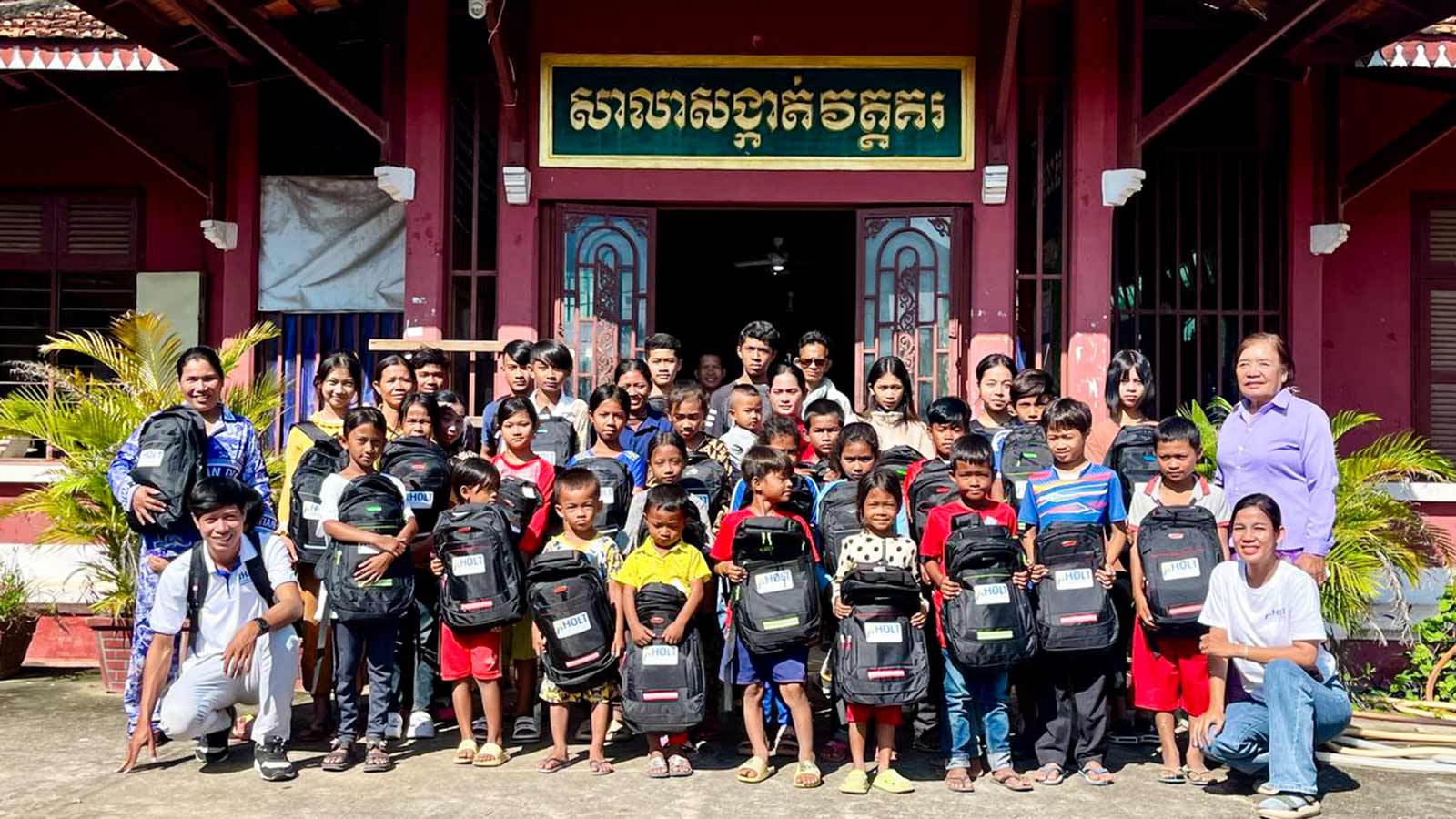children in cambodia hold up their backpacks from Holt sponsors and donors.