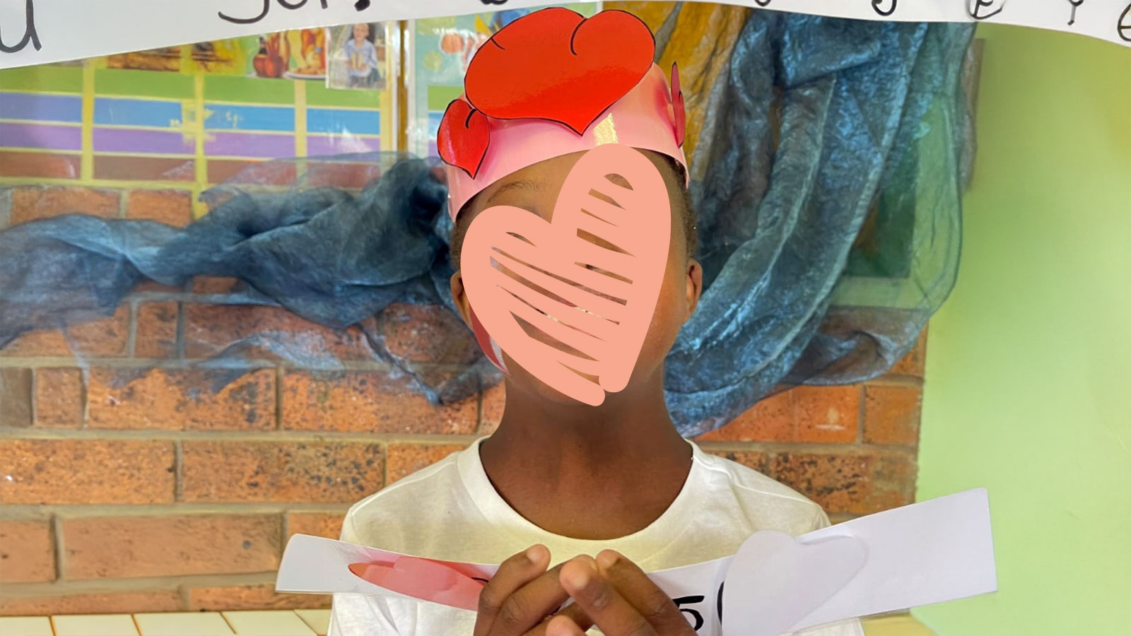 a little girl smiles with a paper crown with hearts on her head, waiting for adoption