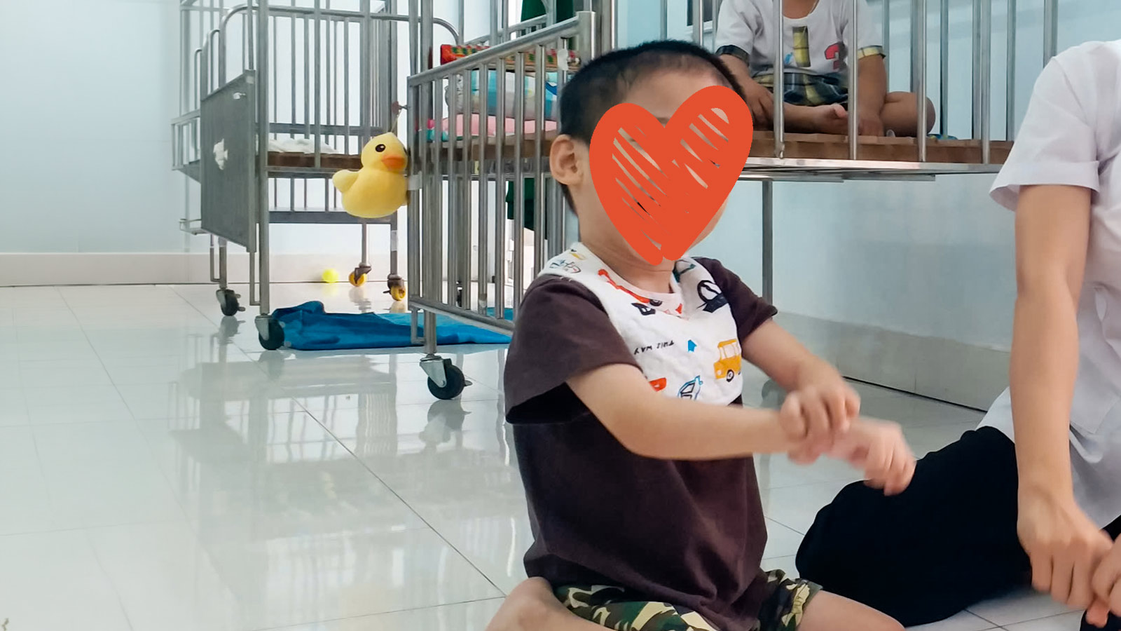 a boy with a red heart over his face sits on white tile and smiles.