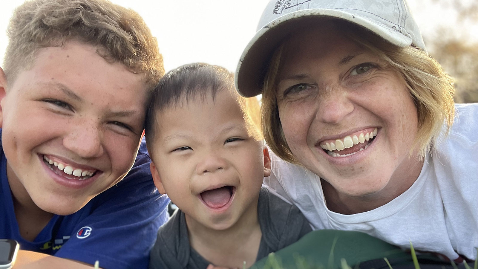 Adoptive mom smiling with bio son and son she adopted with Down syndrome