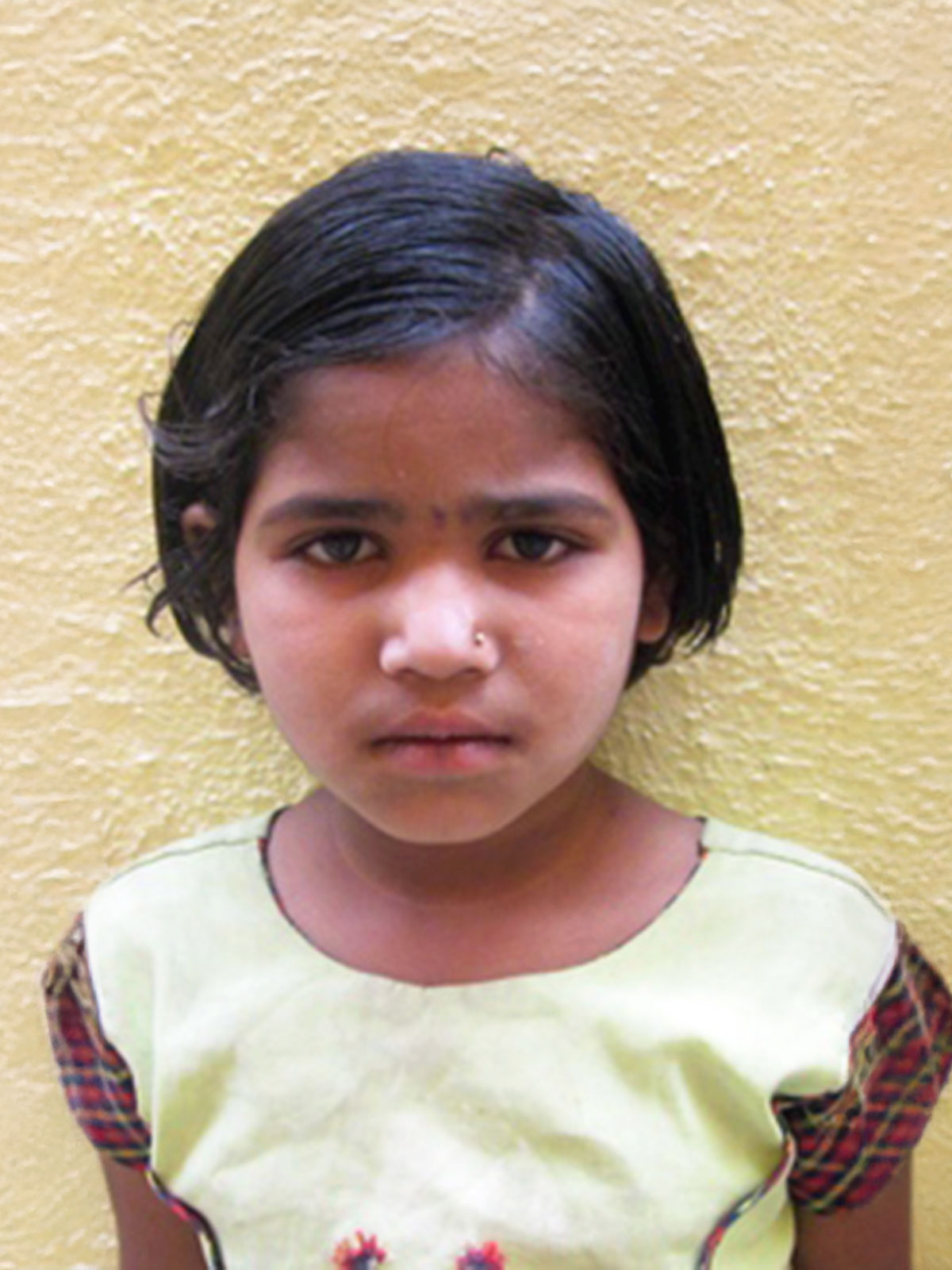 a young girl stands against the wall in India, looking downcast