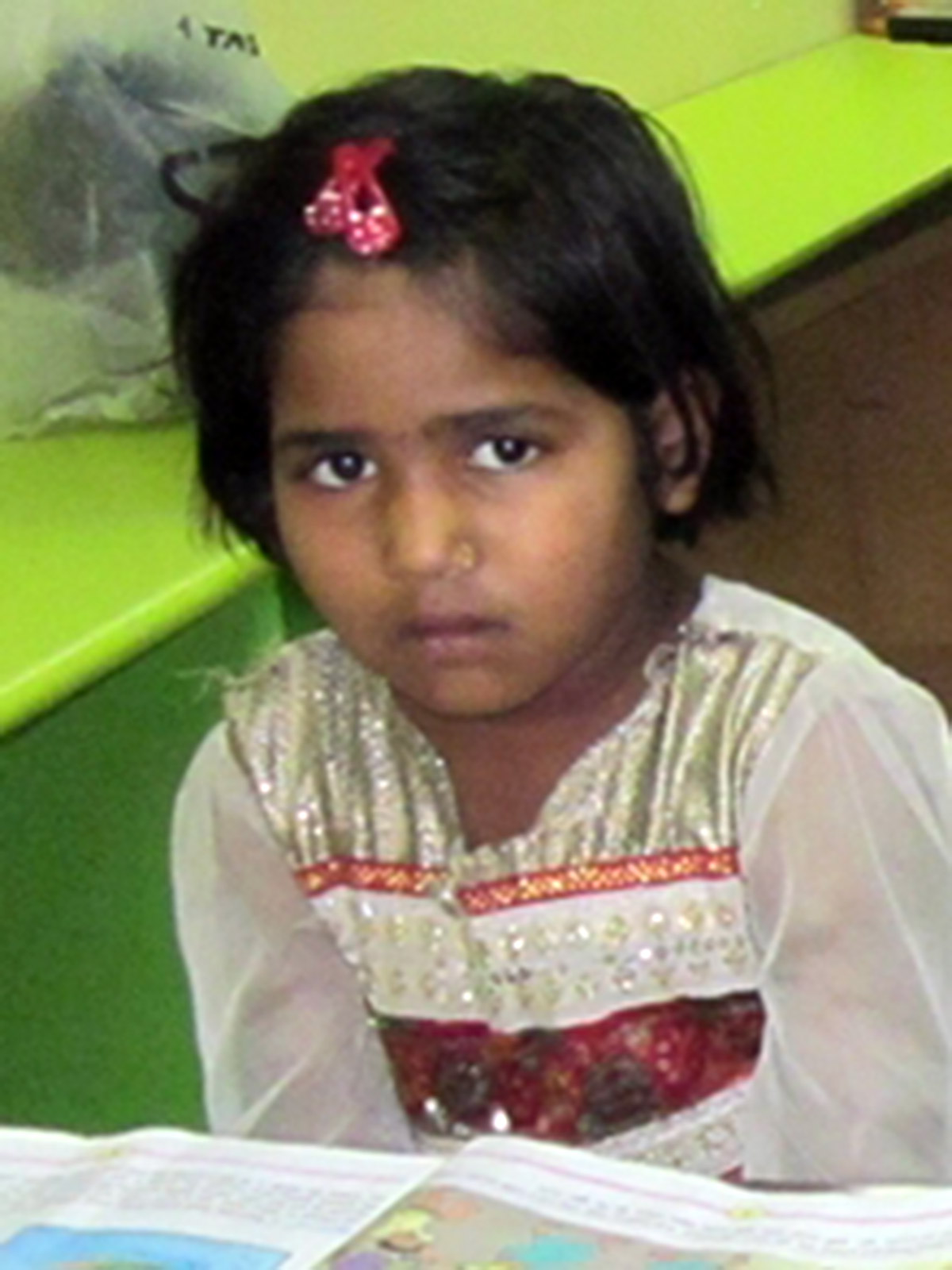 a little girl in India wears a shiny top and looks downcast