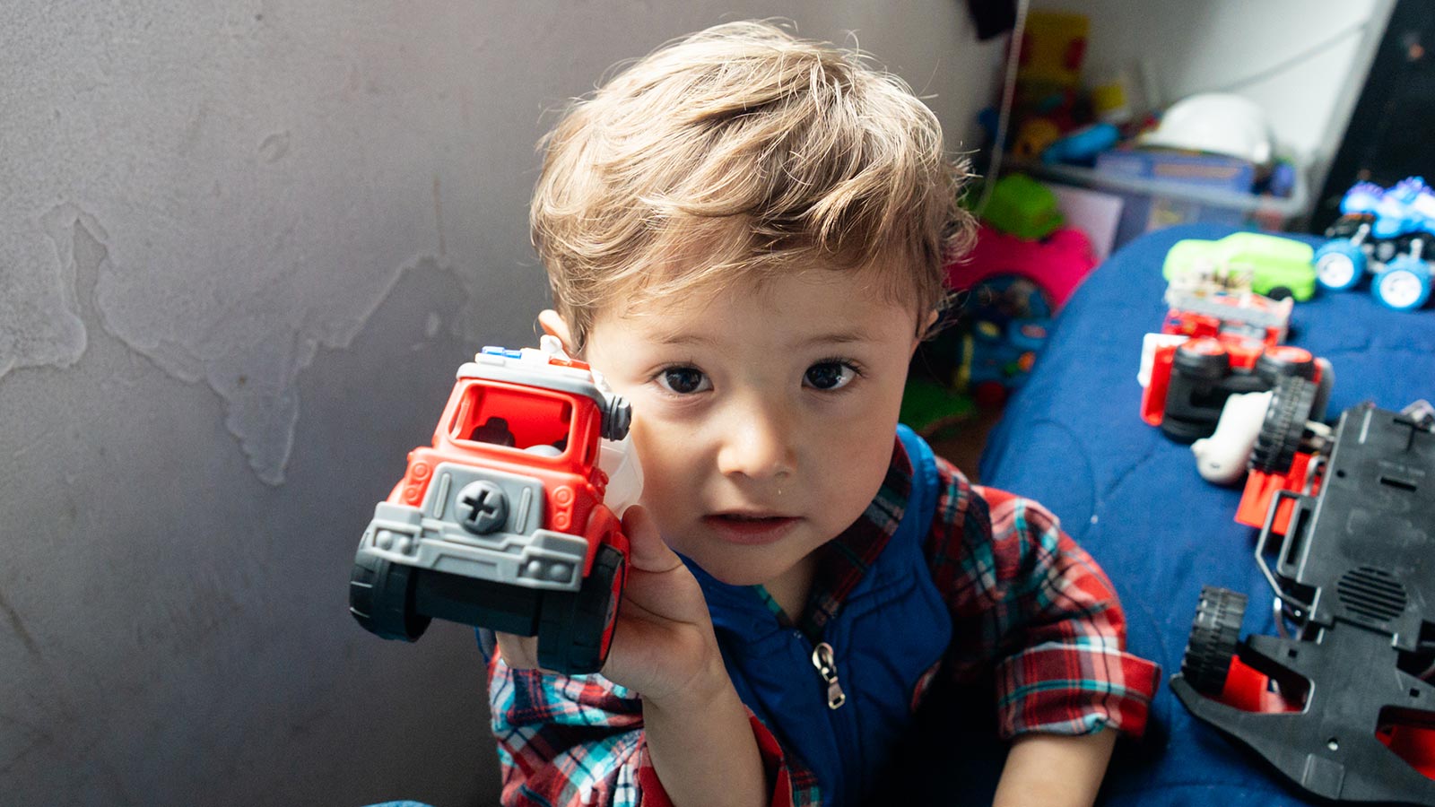 a little boy in colombia holds up a toy fire truck and looks into the camera