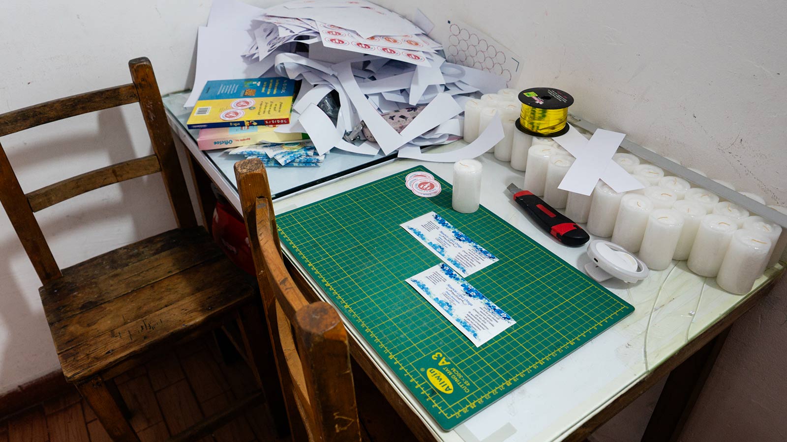 a cutting mat, scraps of paper and some candles sit on a work table