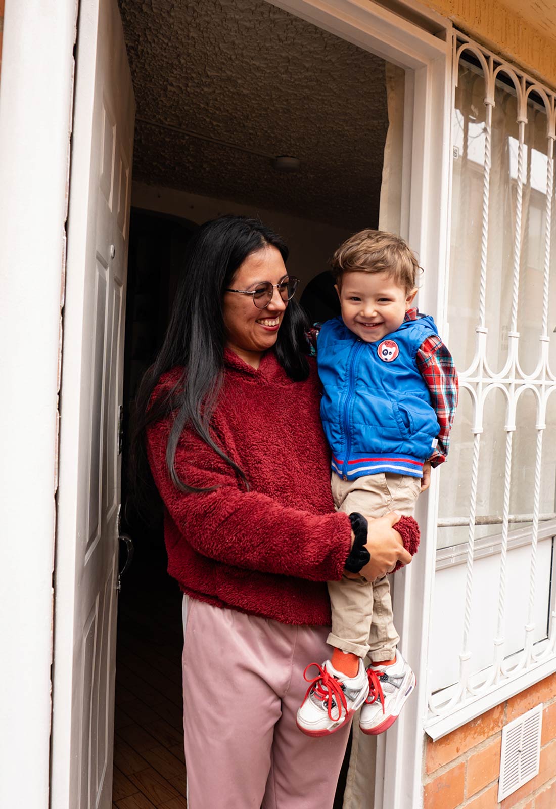 a mom holds her infant son, standing at the doorway of their home in colombia