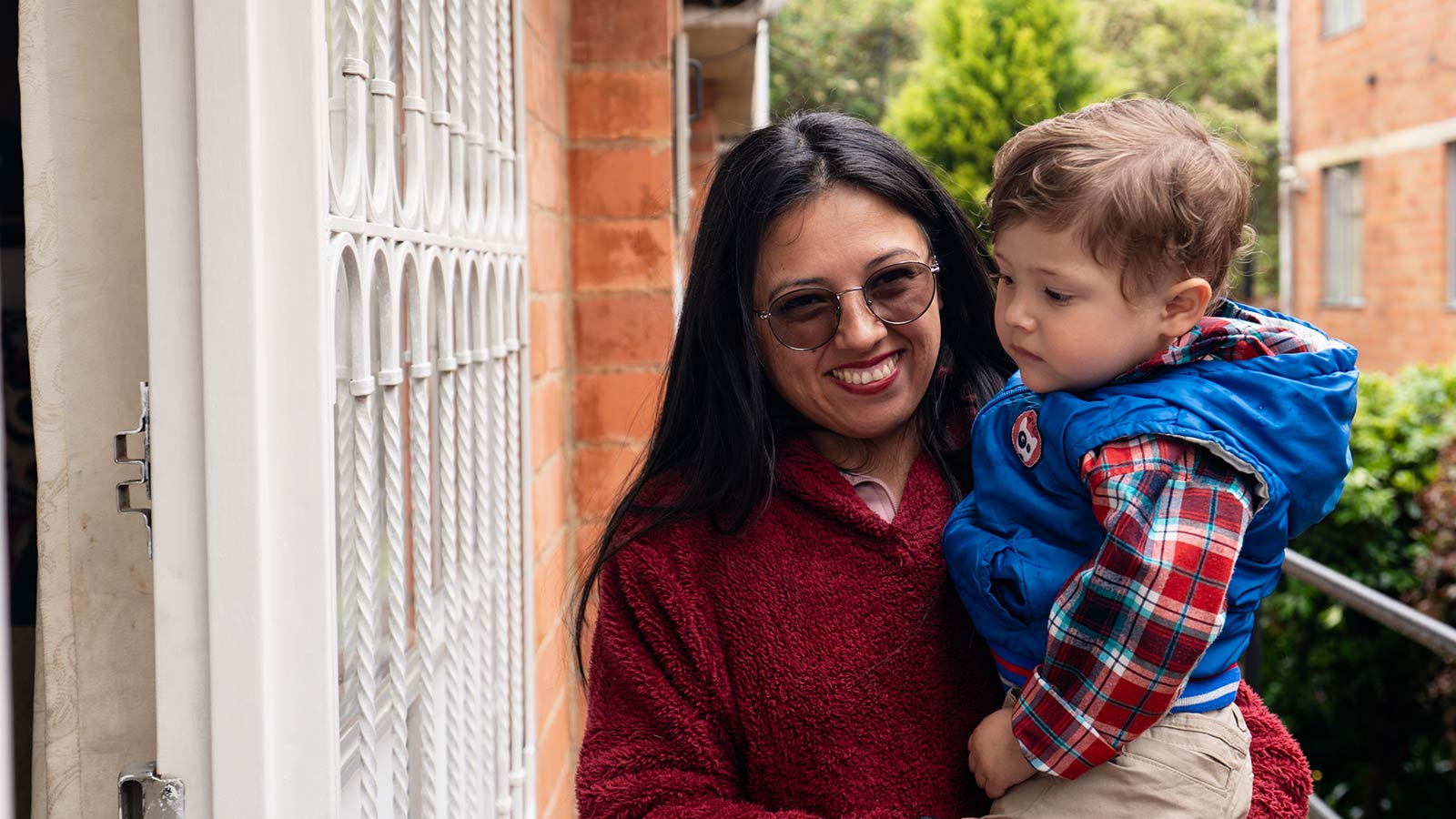 a mom holds her infant son, standing at the doorway of their home in colombia