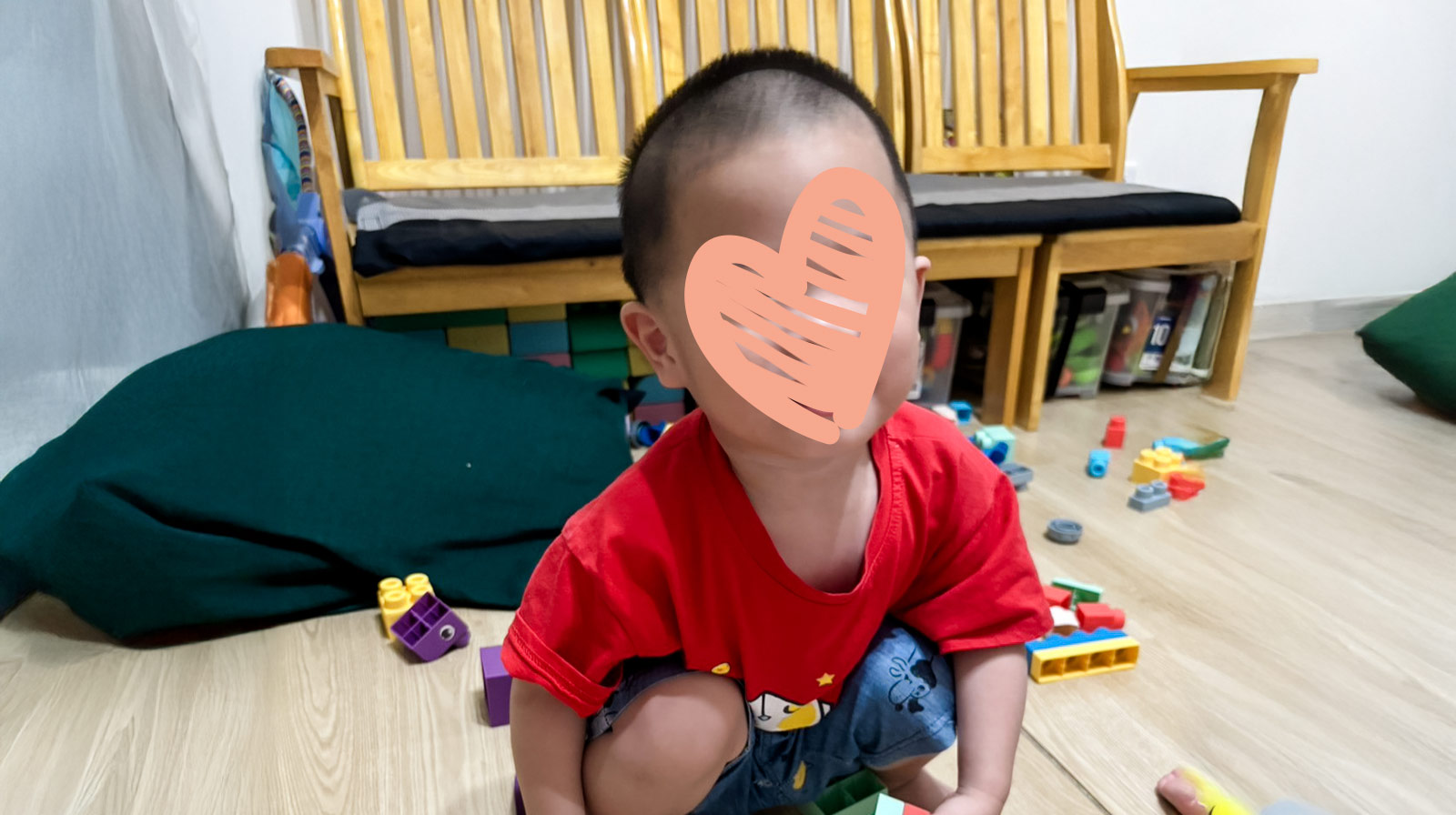 a boy sits on the floor, surrounded by toy blocks. He's waiting for an adoptive family.