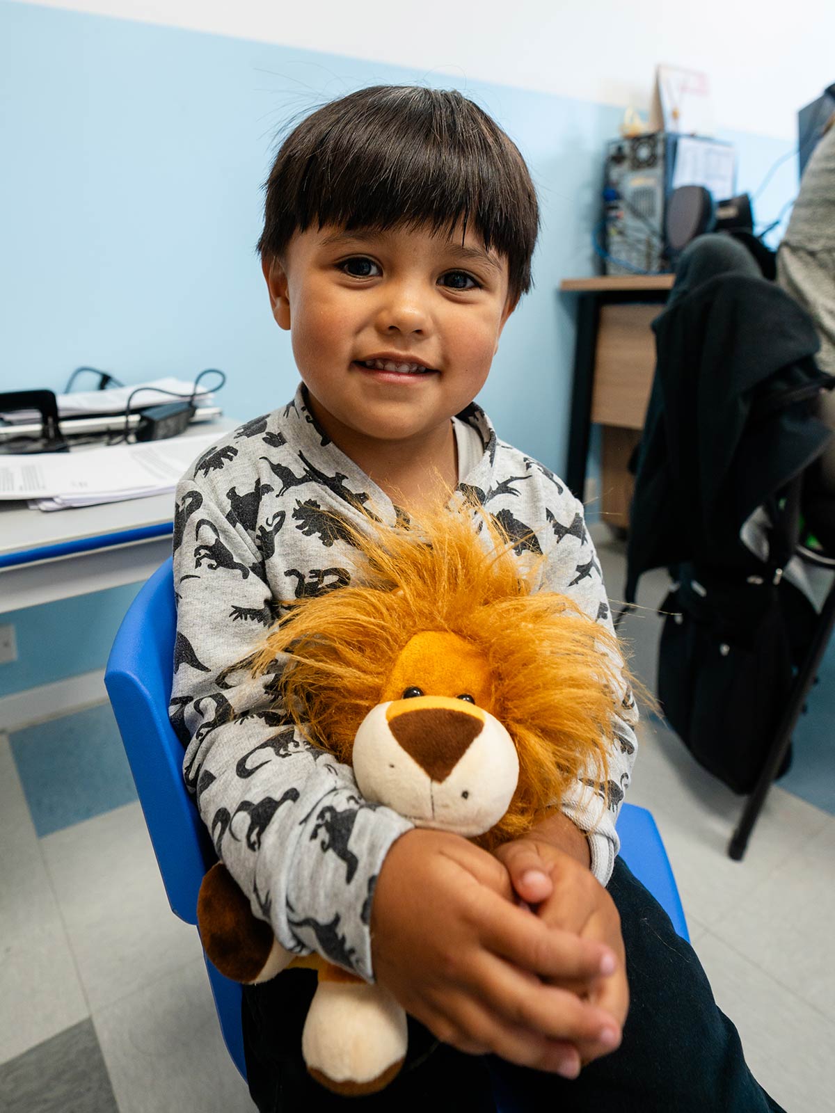 a little boy wearing a dinosaur sweatshirt holds a stuffed lion