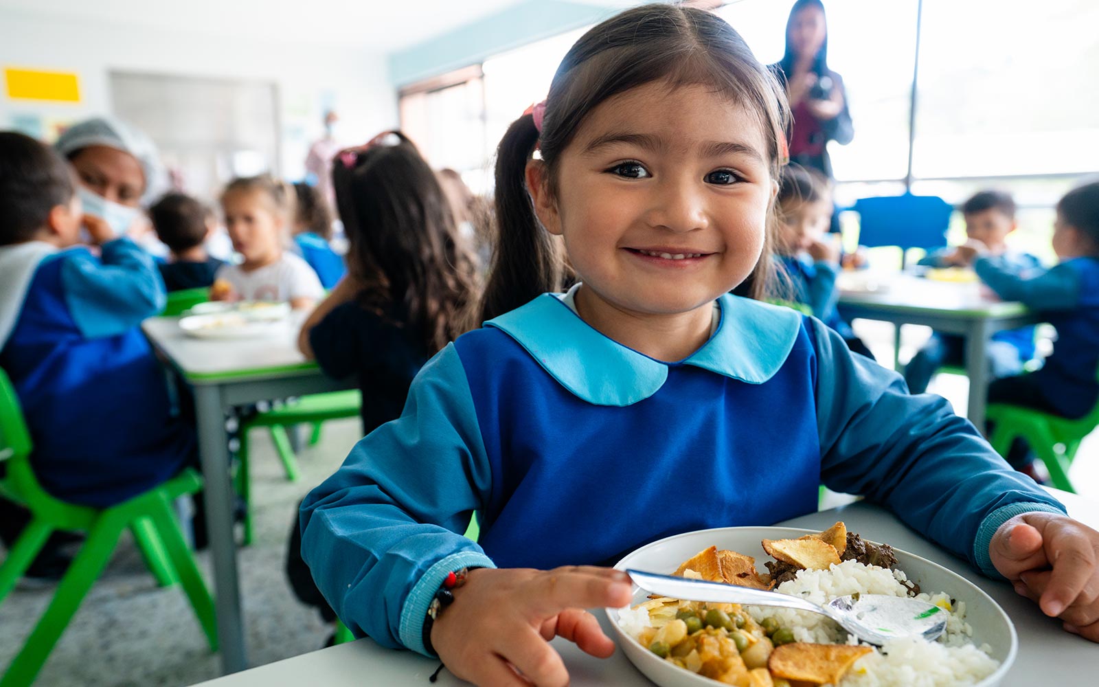 a little girl smiles and eats her lunch at a children's center in colombia