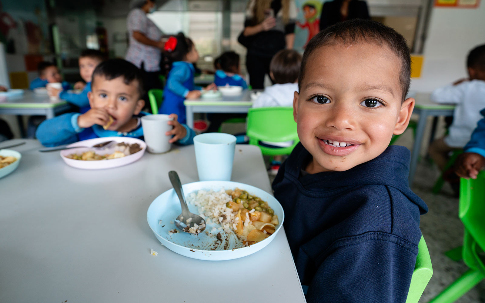 a child smiles next to his plate of lunch at a children's center in colombia