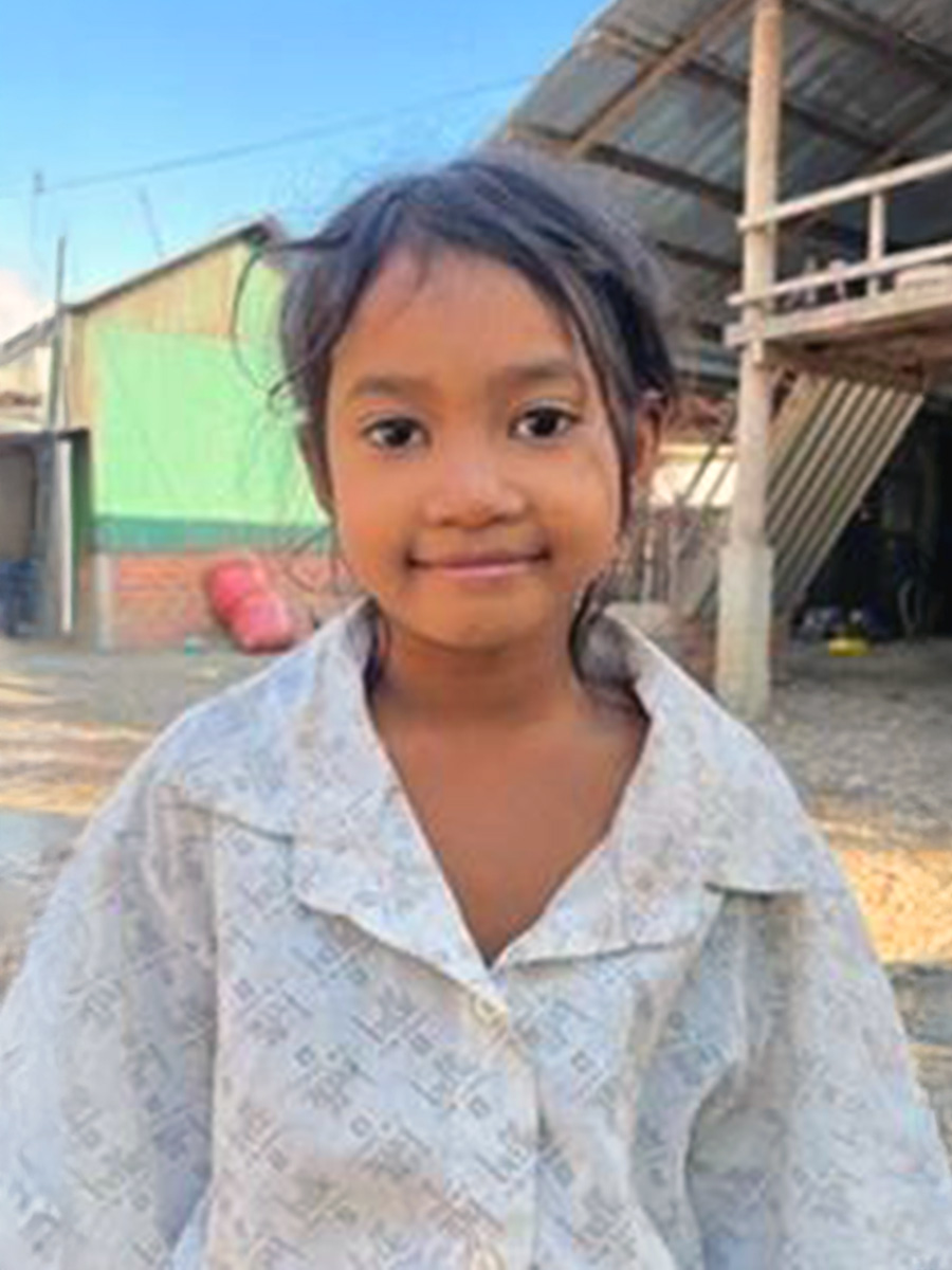 a little girl in cambodia smiles outside her house