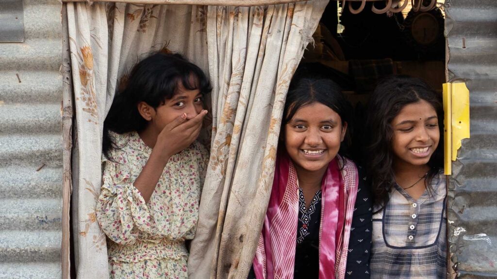 Three girls looking out a window smiling at the camera
