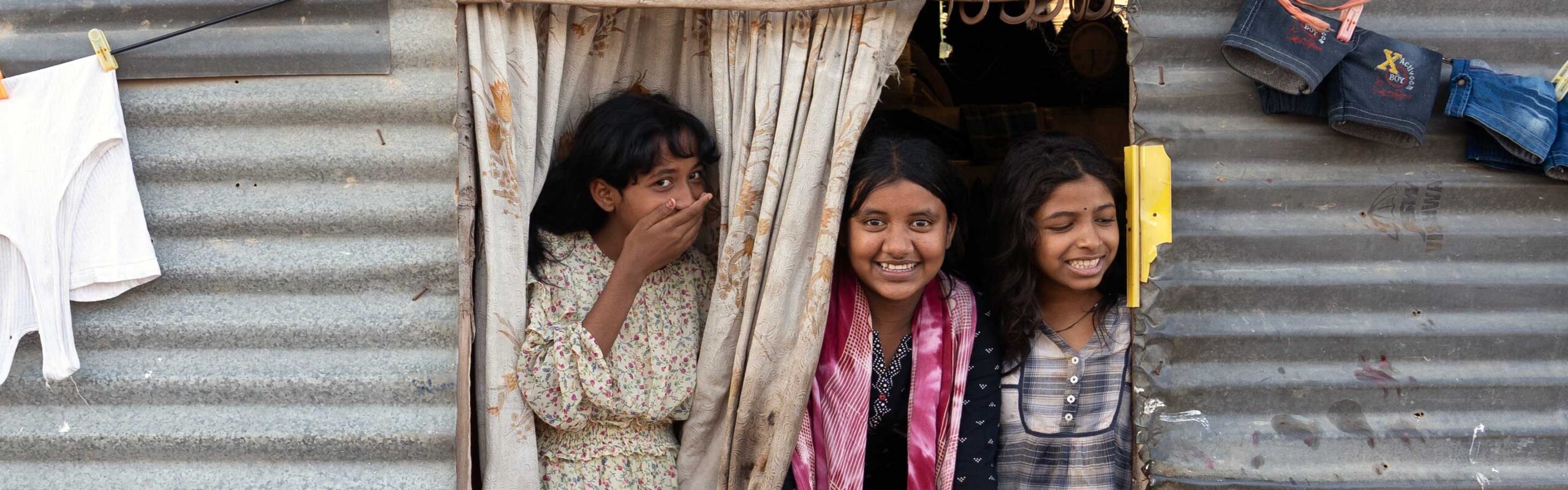 Three girls looking out a window smiling at the camera