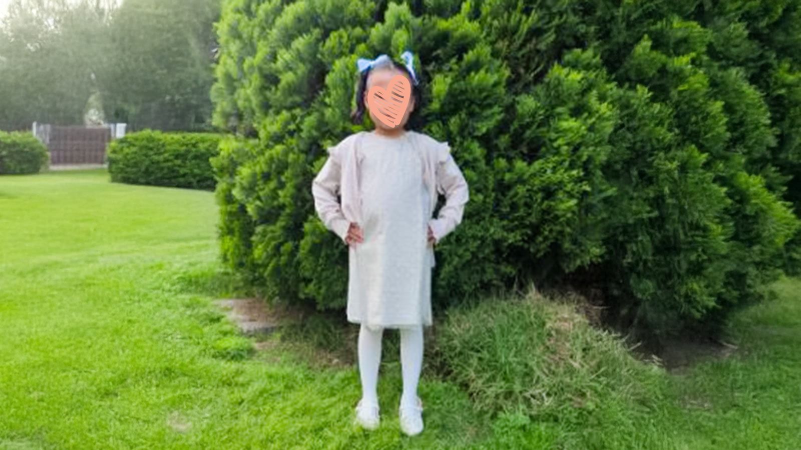 a waiting child stands outside on a lawn wearing a white dress and tights