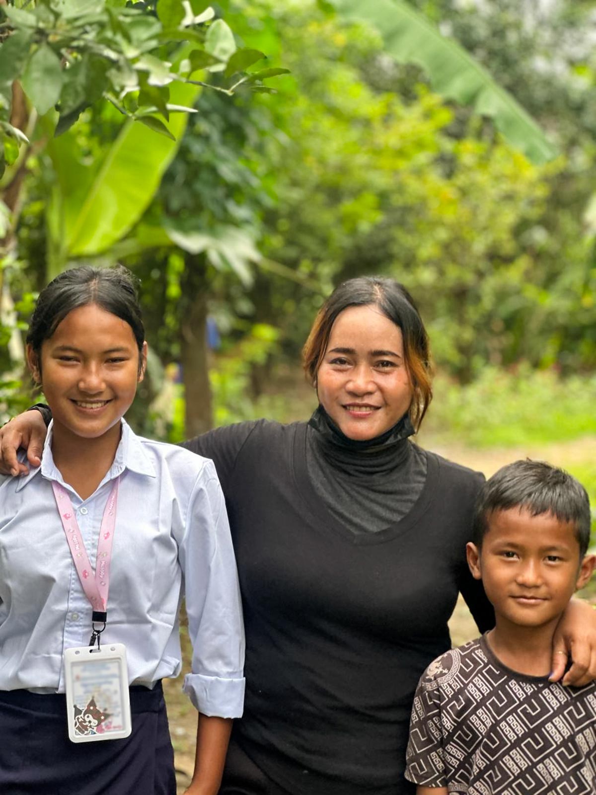 a family of three smiles and holds each other outdoors in Cambodia