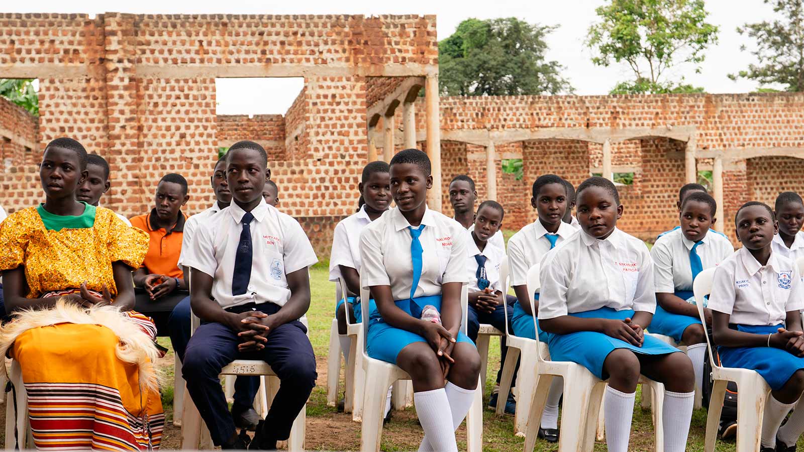 a class of graduates wearing uniforms sits outside on chairs in Uganda