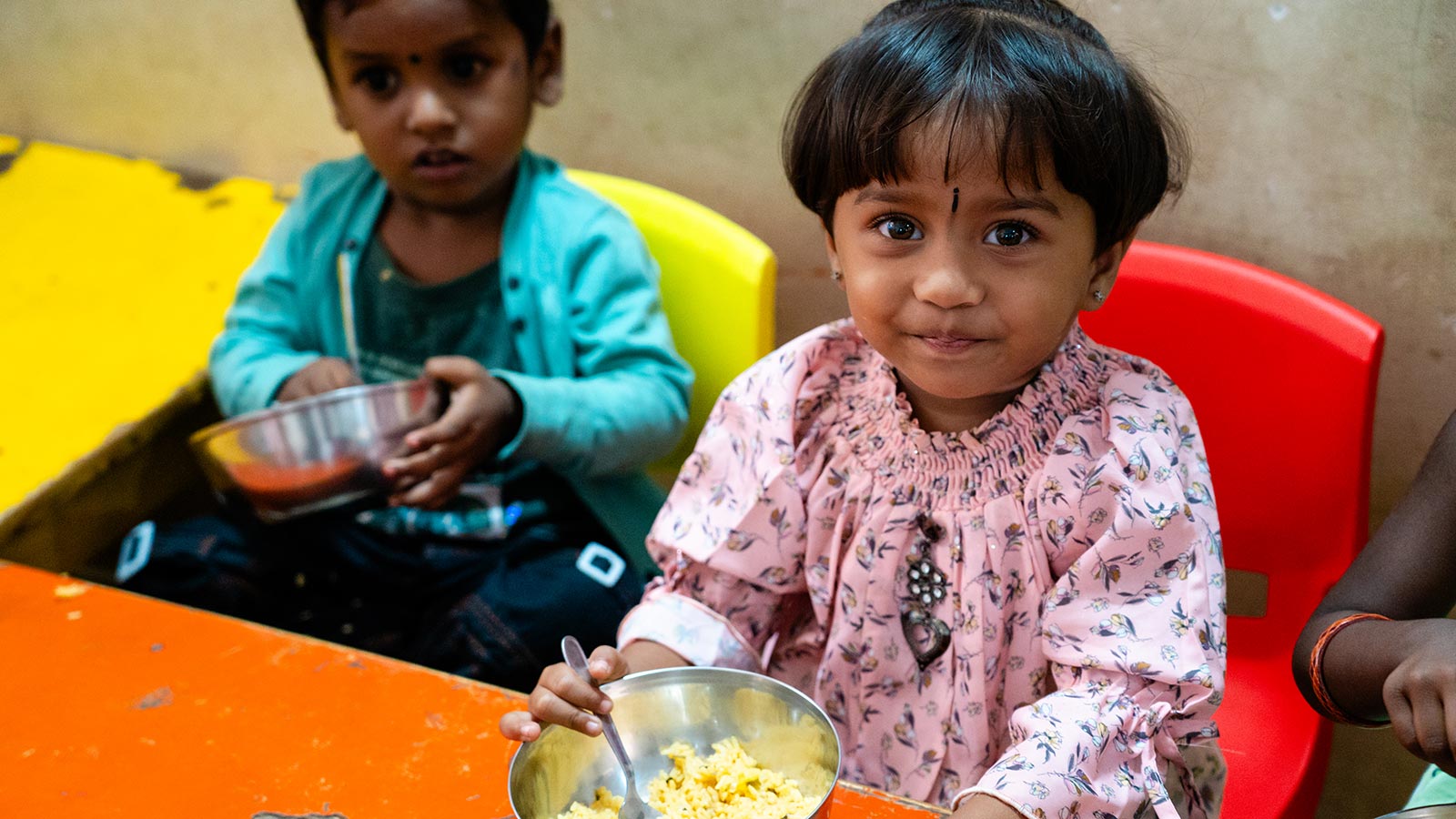 a little girl smiles with her bowl of breakfast at a migrant daycare