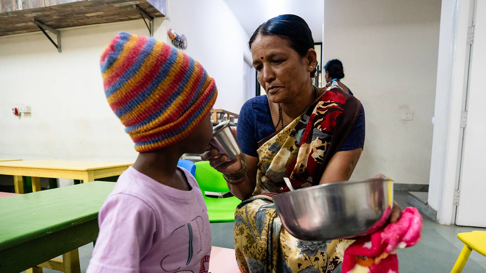 a volunteer holds a tin cup to a little girl's mouth at a migrant daycare