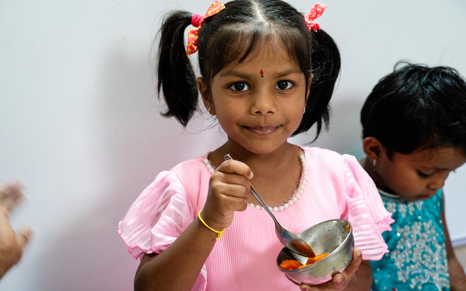 a little girl with pigtails looks at the camera mid scoop from her lunch bowl