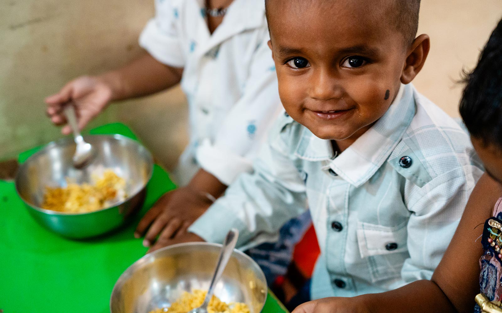 a boy gives a shy smile, sitting at the lunch table with his lunch at daycare