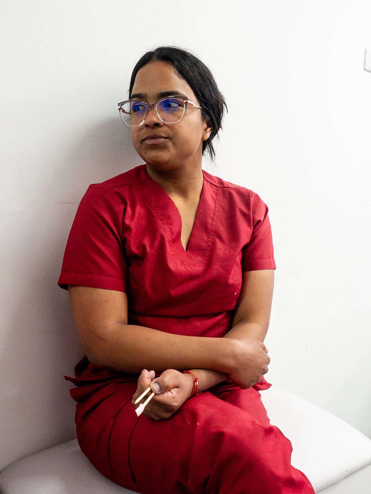 a young woman wearing red scrubs tells her story with a sober expression, holding cuticle sticks