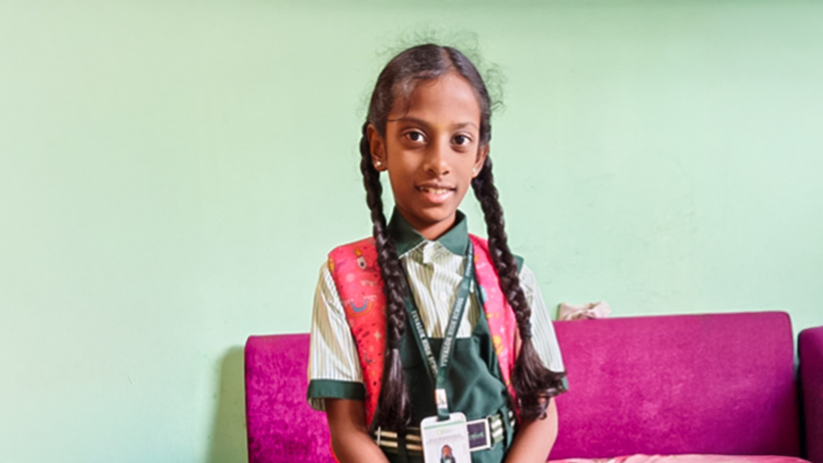 a girl in braids and a school uniform in India smiles