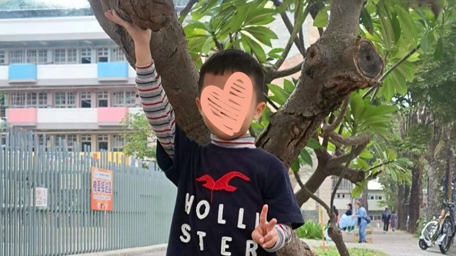 a boy with a heart over his face stands outdoors next to a tree