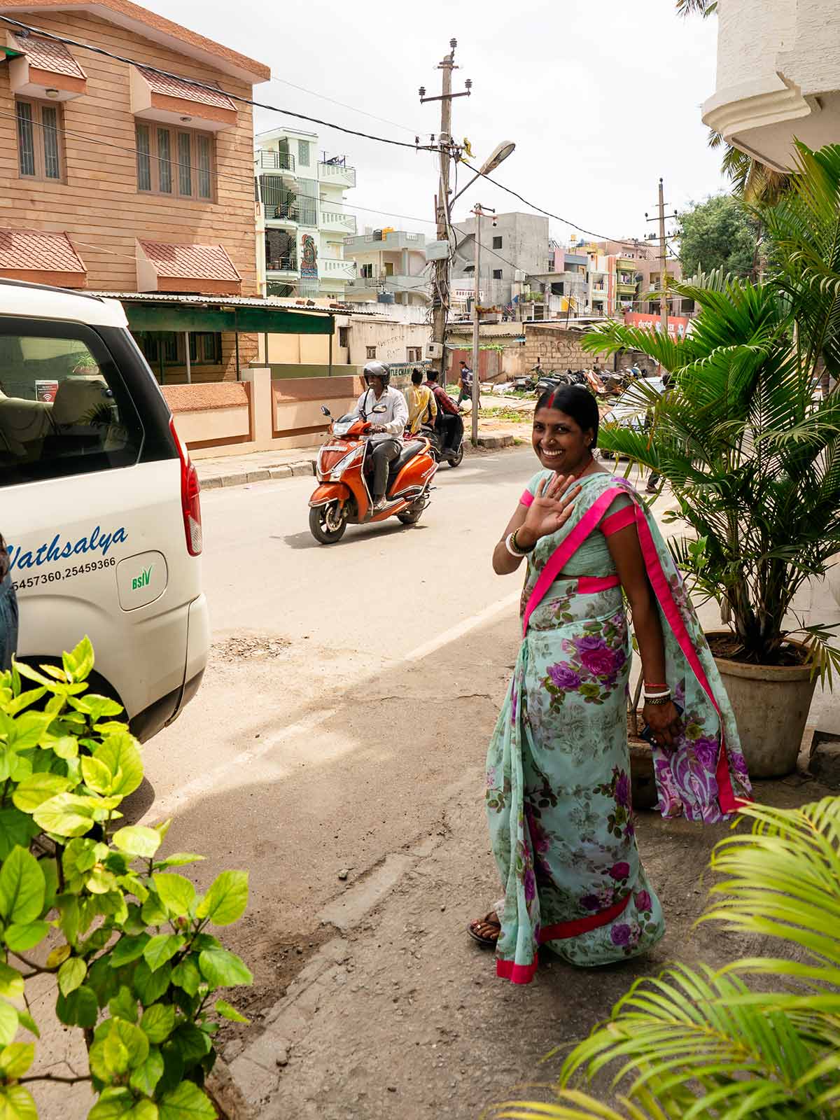 a woman in a floral sari waves goodbye on a street in Southern India