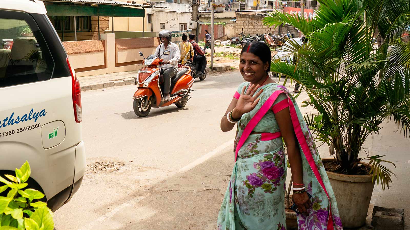 a woman in a floral sari waves goodbye on a street in Southern India