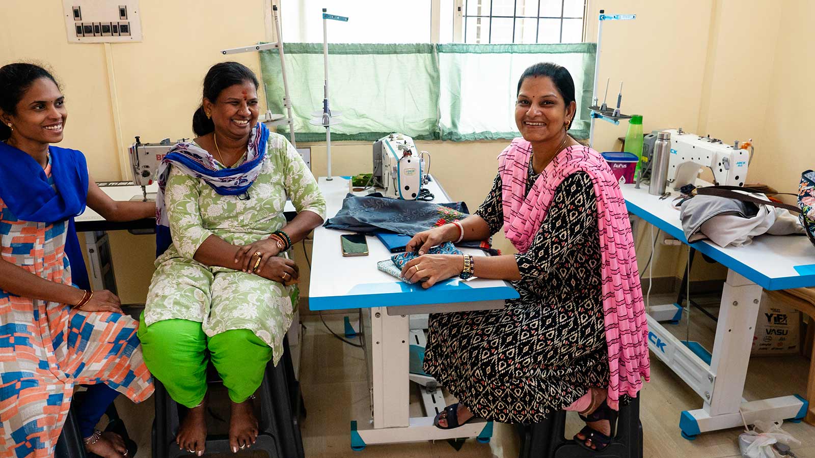 a group of women sit around a sewing machine at a women's center for skills training in India