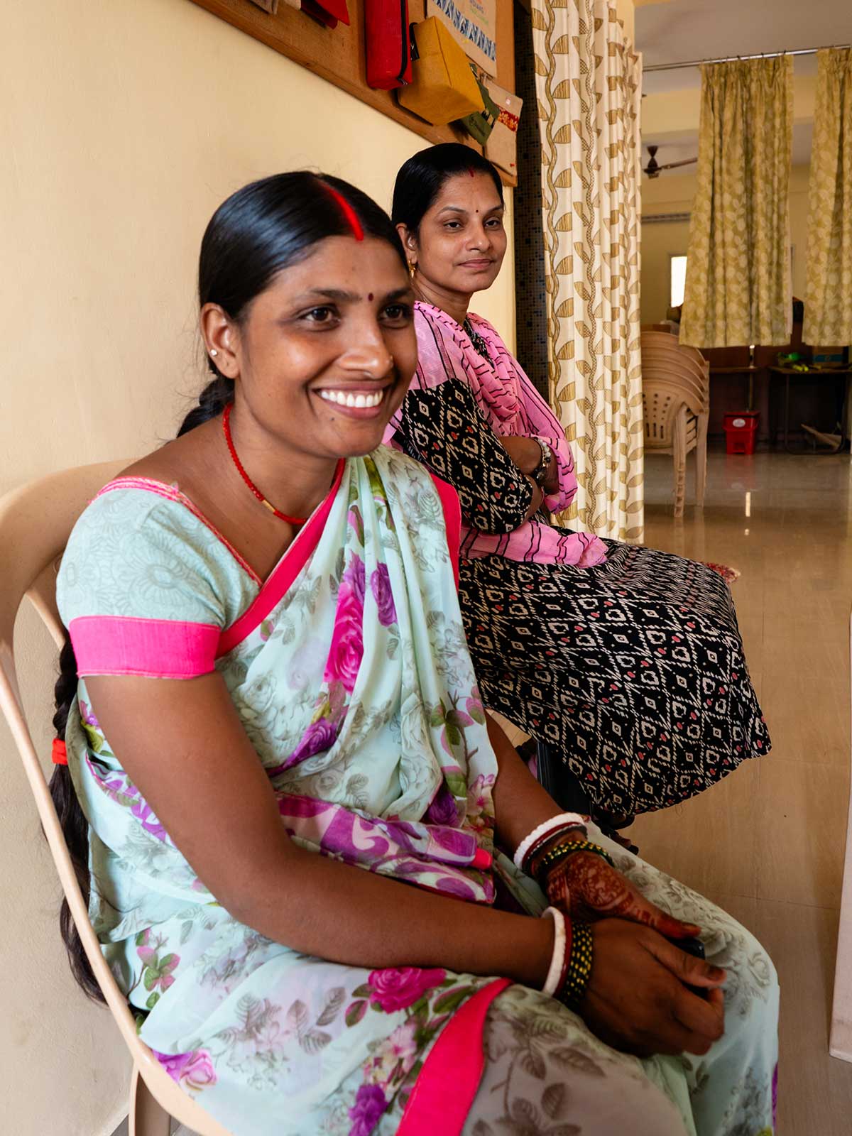 a woman in a floral sari smiles and sits in a women's center in Southern India