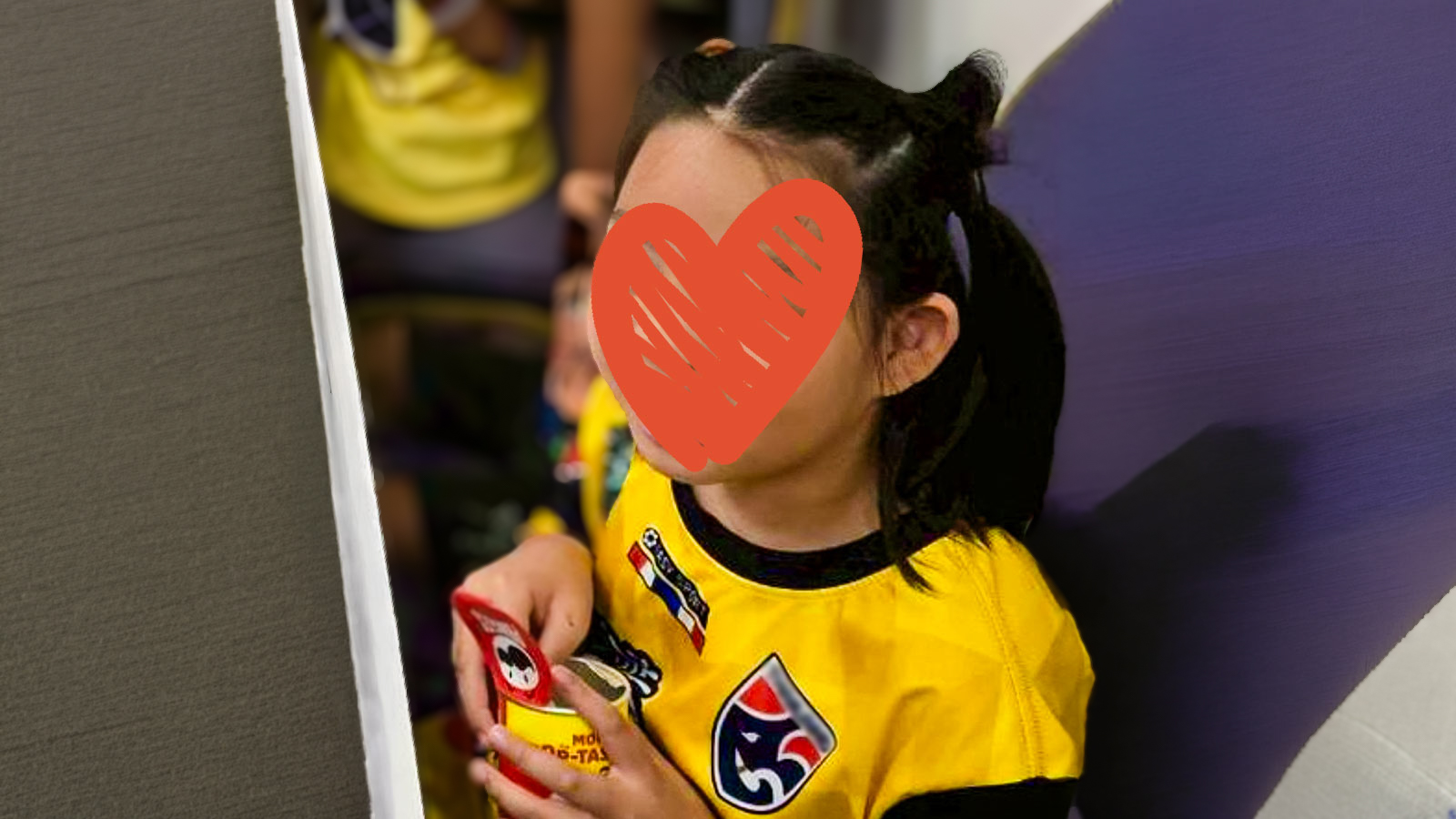 a girl with a yellow soccer jersey and pigtails eats a snack