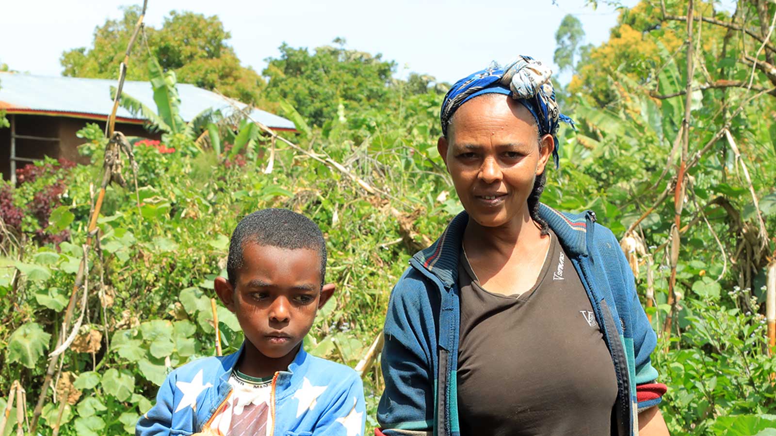 a mother and her son in Ethiopia stand outside in their garden