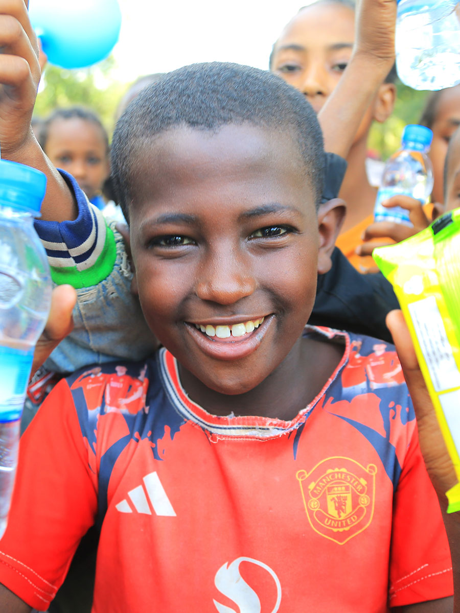 a boy in a red shirt smiles at a birthday celebration in Ethiopia