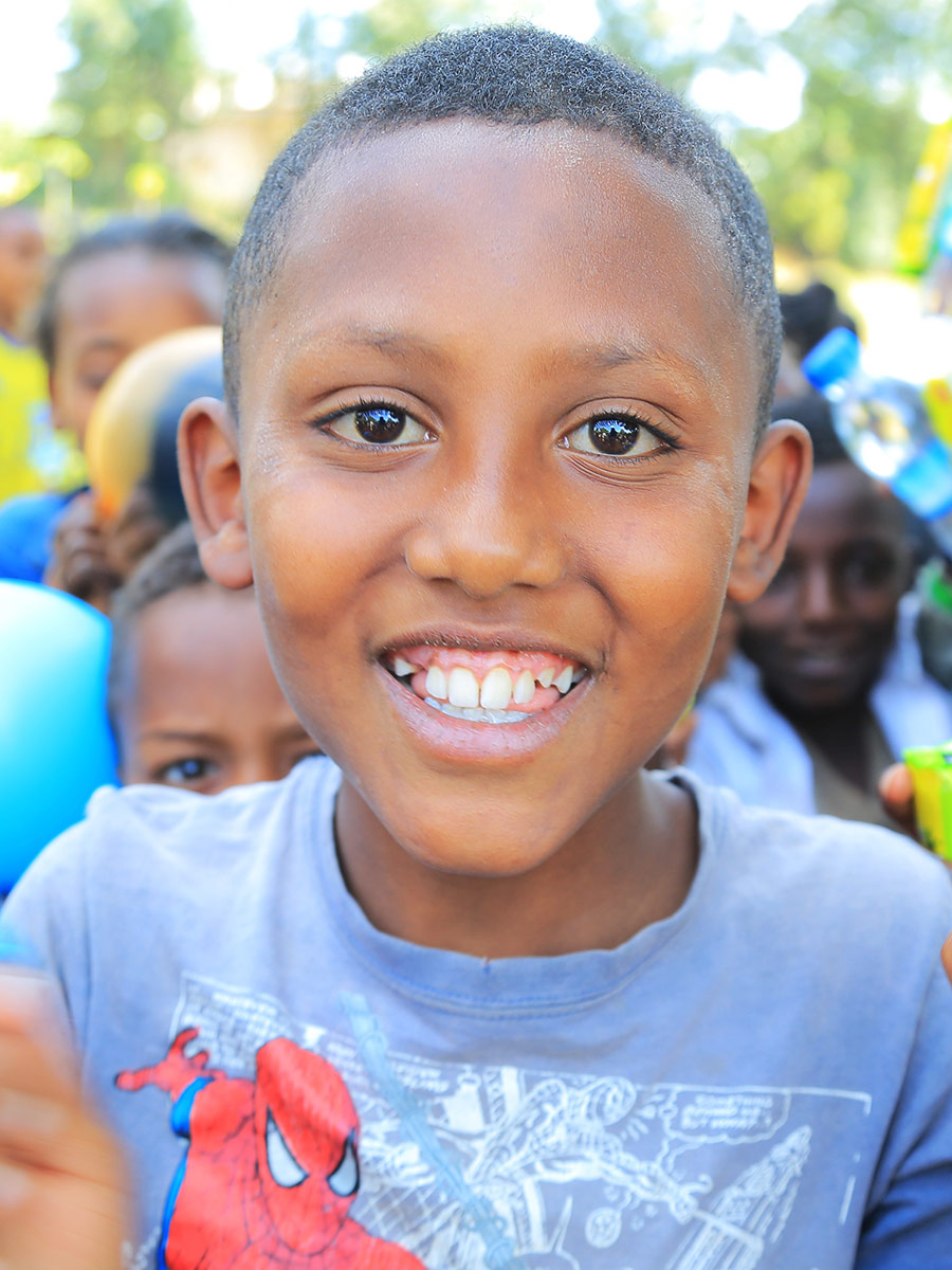 a boy in a grey shirt smiles at a birthday celebration in Ethiopia