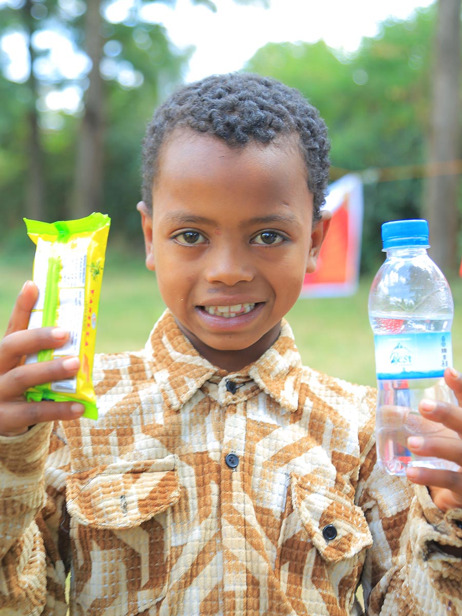 a boy in a brown shirt smiles at a birthday celebration in Ethiopia