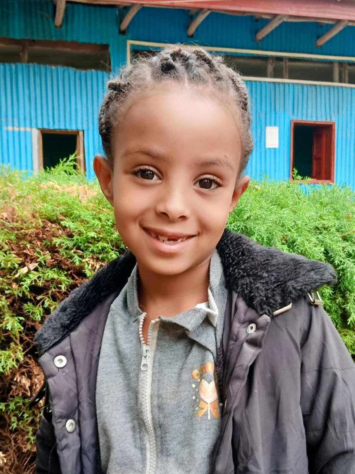 In Ethiopia, a girl with braids smiles outside of her preschool classroom
