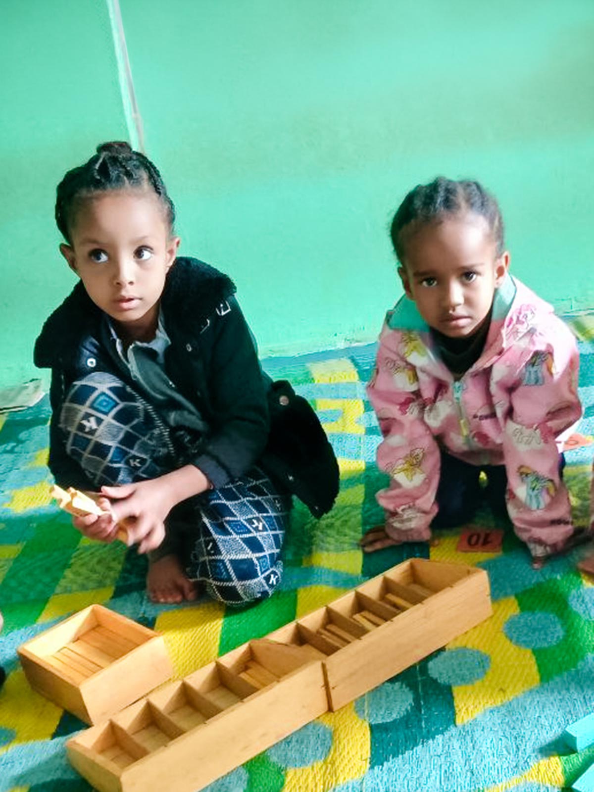 In Ethiopia, two girls play with wooden blocks on the floor in their preschool classroom