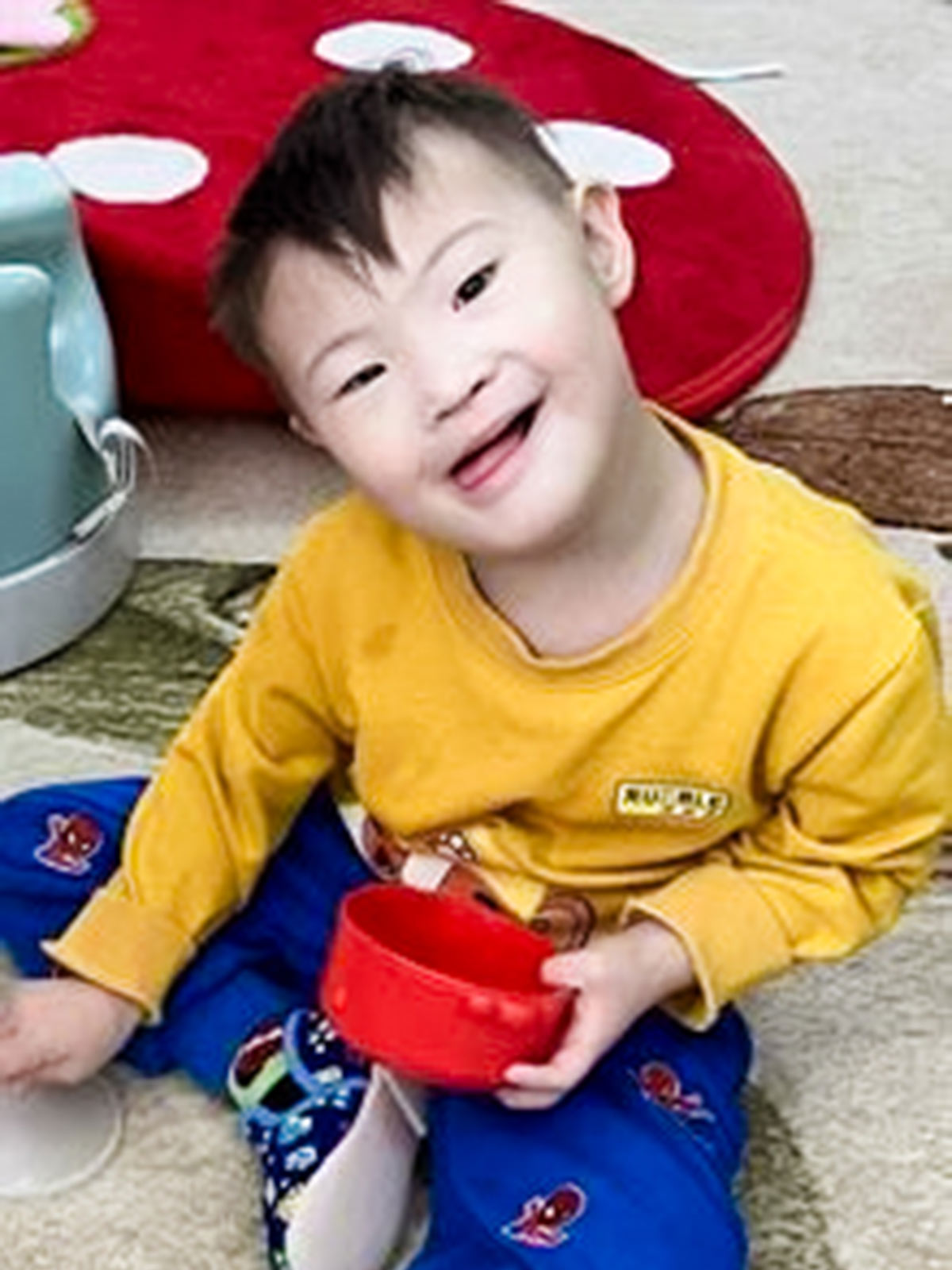 a sponsored child in a yellow shirt and blue pants smiles into the camera
