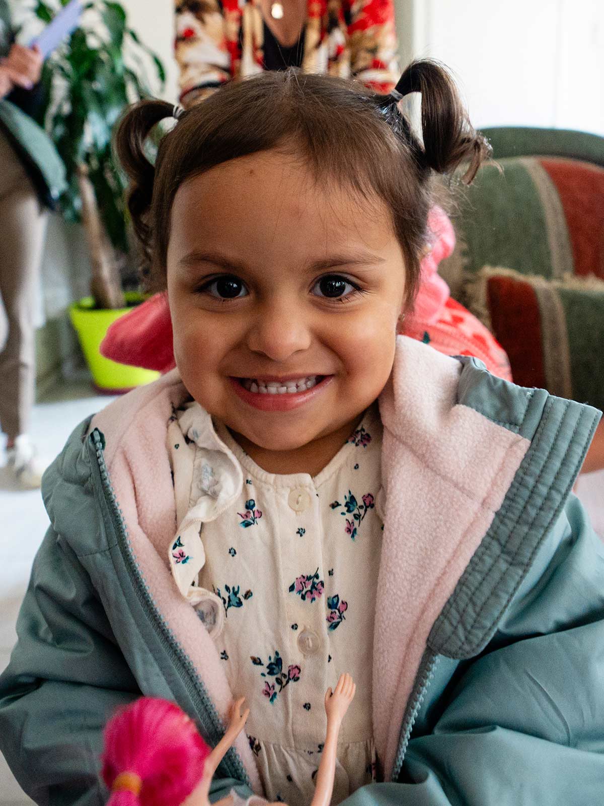 a toddler with pigtails smiles while holding a doll