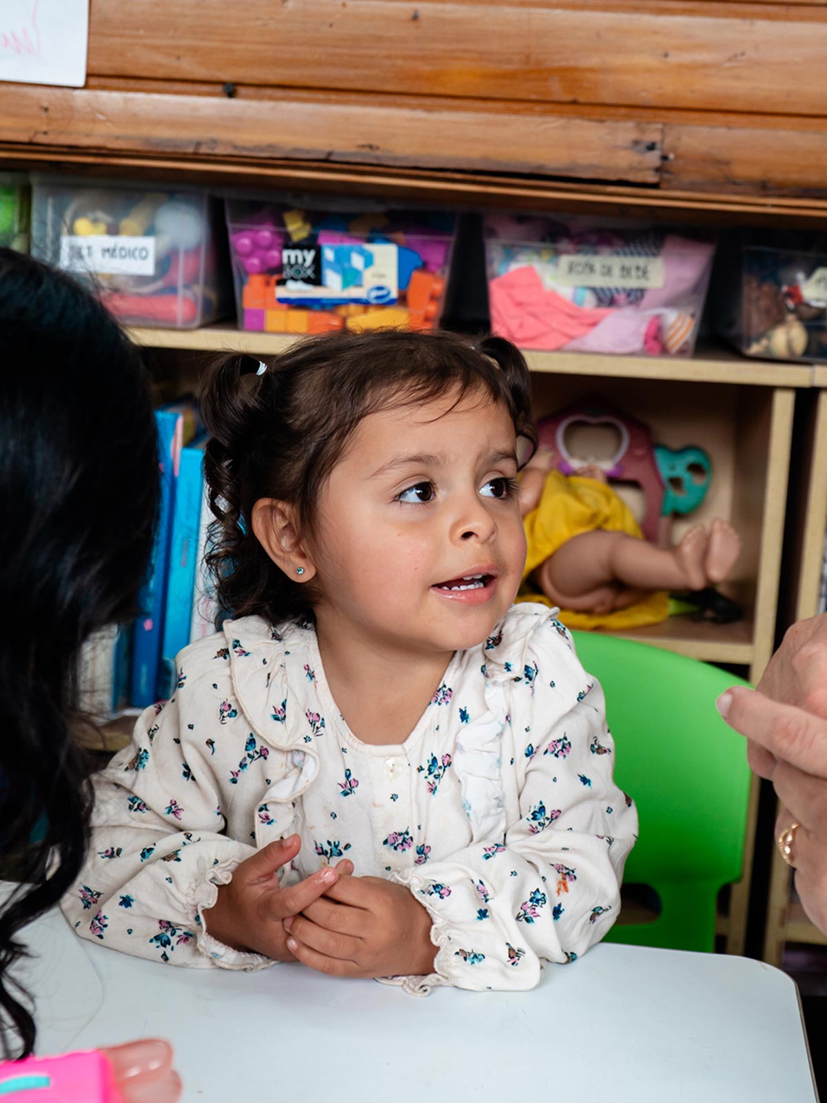 a young girl with pigtails sits with her family at La Casa de la Madre y el Niño