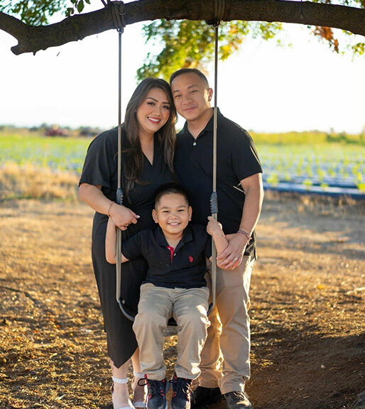 Thien sits on a swing while his parents stand behind him