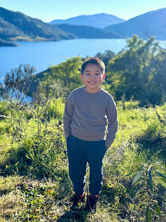 Thien stands on a hill wearing a gray sweater and pants