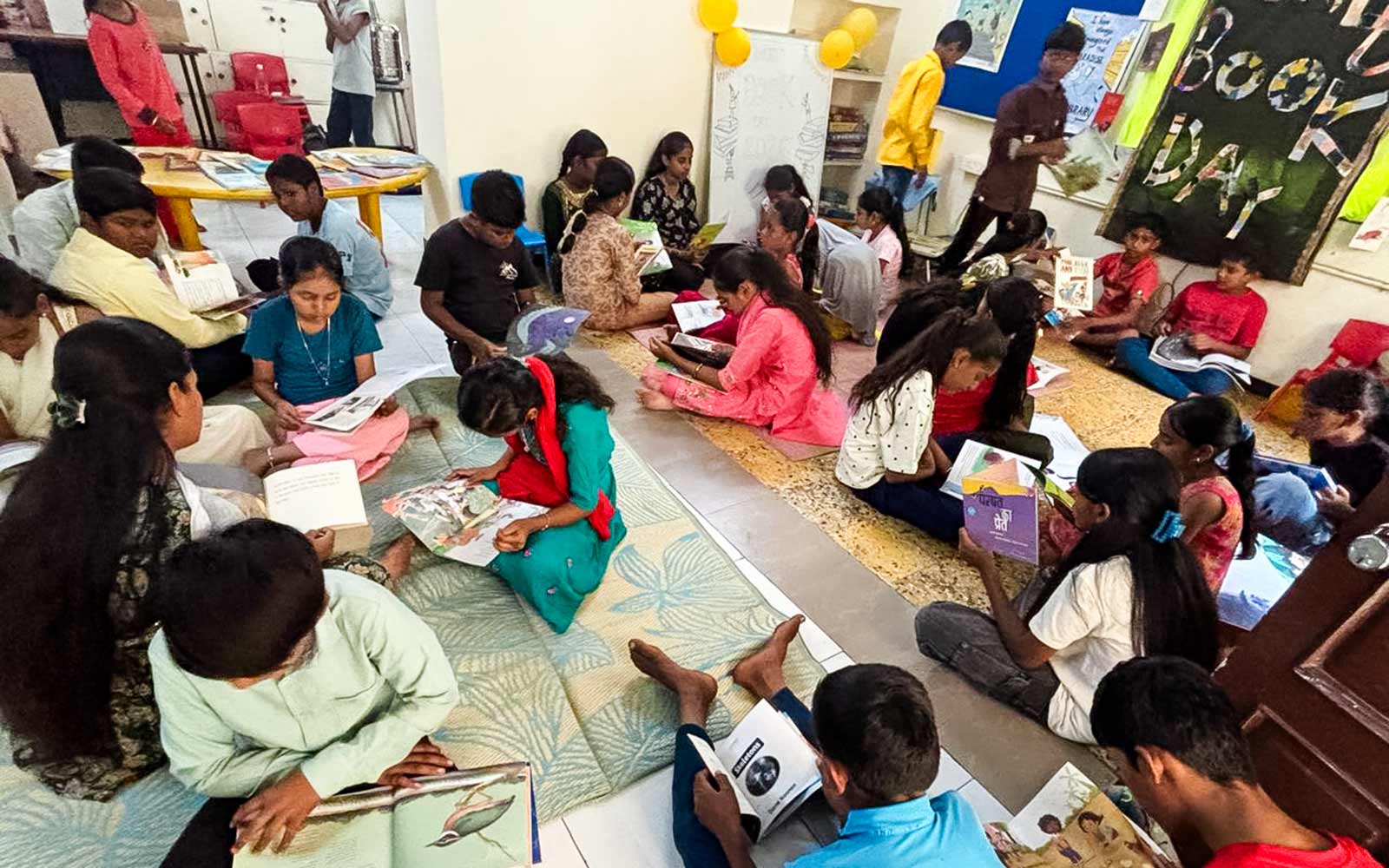 a room full of children read books on the floor of a BSSK library center in India for world book day